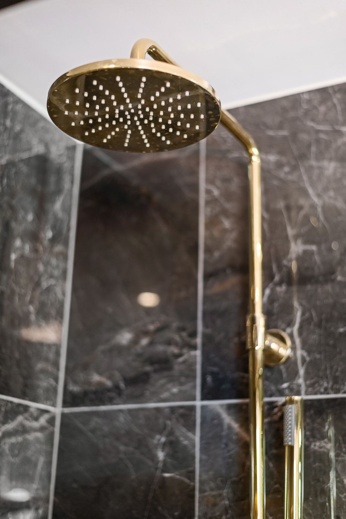 Brass rain shower against dark marble tiles